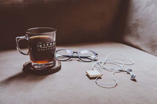 coffee clear Brain printed glass mug on brown wood slab coaster beside black framed eyeglasses and white earphones coffee cup