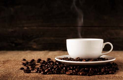 coffee white ceramic mug and saucer with coffee beans on brown textile coffee cup