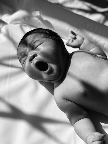 person grayscale photo of baby on bed black-and-white