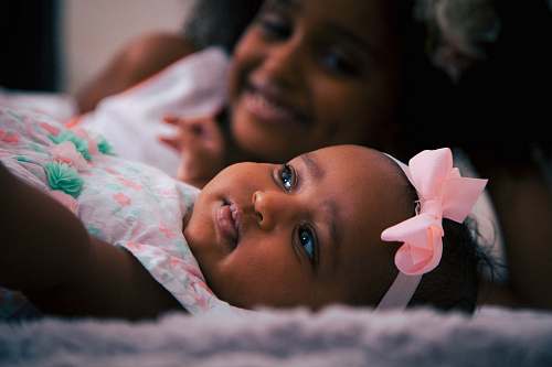 person toddler wearing white and pink headdress lying near girl baby