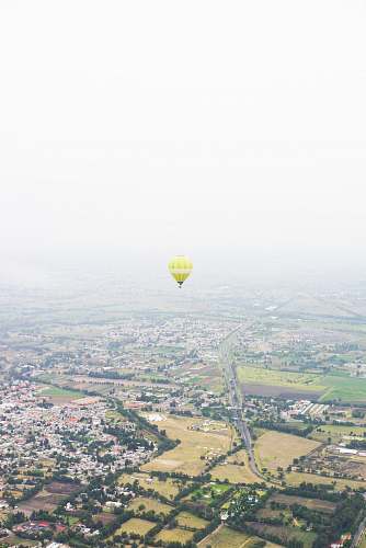 sky photo of yellow hot air balloon floating above houses hot air balloon