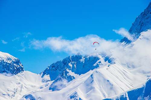 nature photo of person with parachute above snowy mountain snow