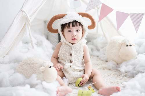 person baby sitting beside white sheep plush toy human