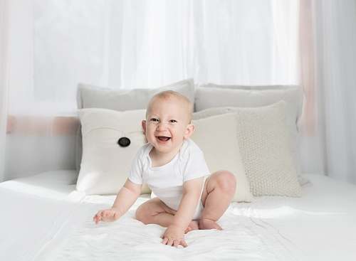 cushion smiling baby sitting on white bed pillow
