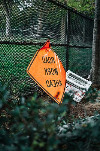 road work ahead signage leaning on chain link fence