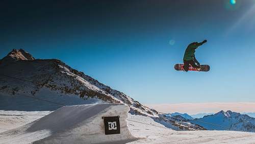 sport person wearing green jacket jumping on white snow ramp during daytime snow