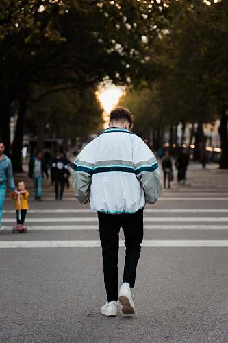 tarmac man wearing white and blue jacket and black jeans walking on street road