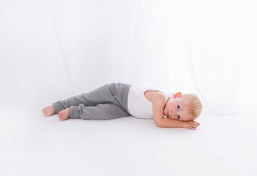 human boy wearing white tank top lying on white surface close-up photography person