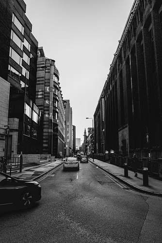 city grayscale photo of vehicles on street between buildings black-and-white