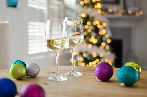 glass two clear footed wineglasses filled with yellow liquid near assorted-color ball ornaments goblet