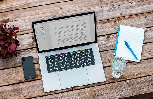 laptop silver MacBook beside space gray iPhone 6 and clear drinking glass on brown wooden top work