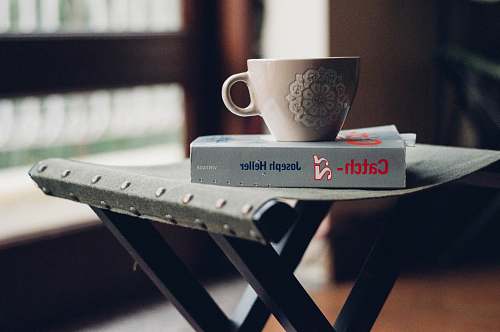furniture close-up photography of beige ceramic coffee cup on top of Joseph Heller book table