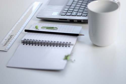 office black pencil on ruled notepad beside white ceramic mug and gray laptop computer work
