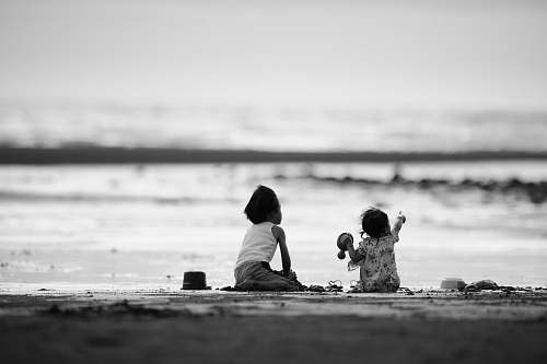 person grayscale photography of two girls sitting on shore black-and-white