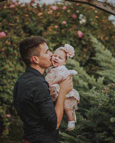 person men holding a baby near plants during daytime clothing