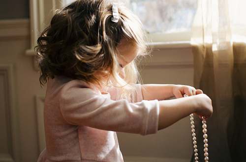 human girl holding white pearl necklace inside room people
