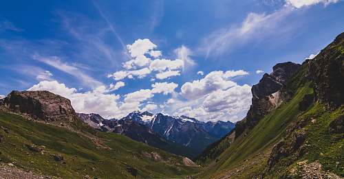 nature green and gray mountain under white and blue cloudy sky outdoors