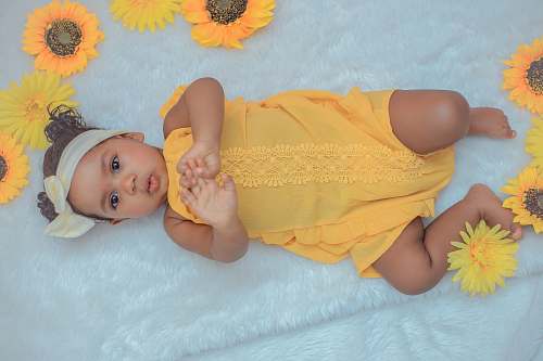 human baby in yellow dress lying on white textile diaper