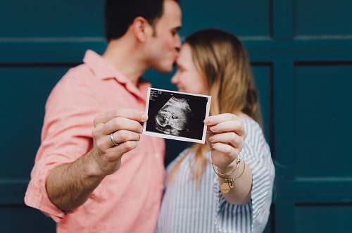 person man kissing woman's forehead white holding ultrasound photo human