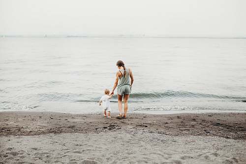 person woman and baby walking on gray sand seashore during daytime human