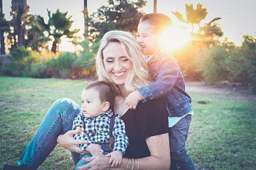 family woman holding baby sitting on green grass field under sunset woman