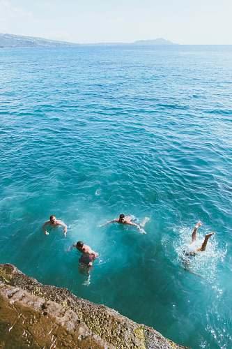 water aerial photography of four men swimming in blue sea human