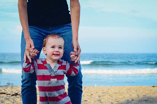 beach man assisting baby to walk on beach ocean