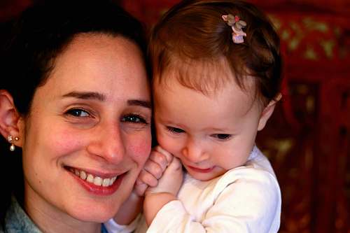 human smiling woman in blue top cuddling baby finger