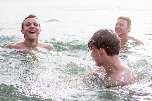 water three men smiling while swimming during daytime swimming