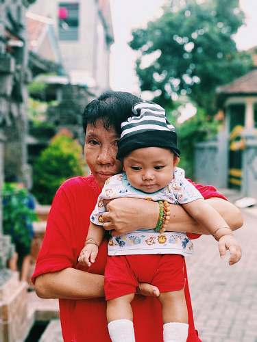clothing woman carrying a baby near houses at daytime apparel
