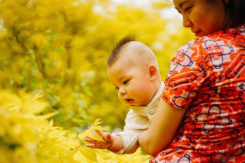 human woman in orange, white, and black floral short-sleeved shirt holding baby baby