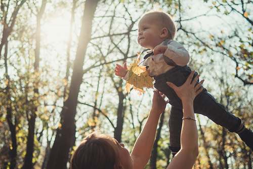 leaf close-up photography of woman carrying a baby near outdoor during daytime tree