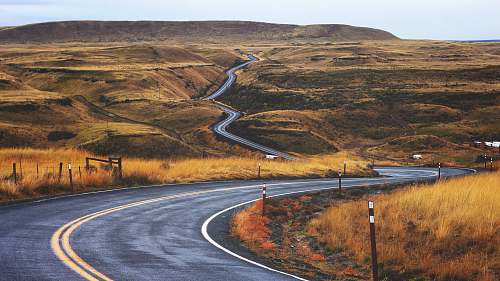 hills gray concrete road across brown valley during daytime travel