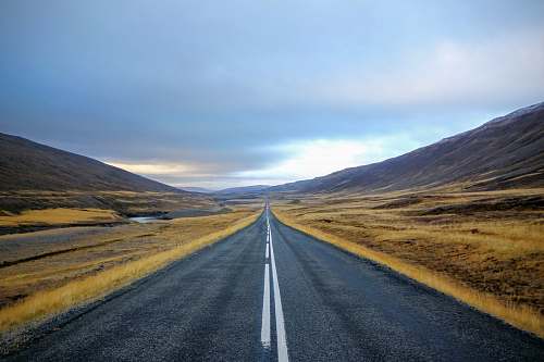 freeway landscape photography of black asphalt road with white line surrounded by brown grass field during daytime iceland