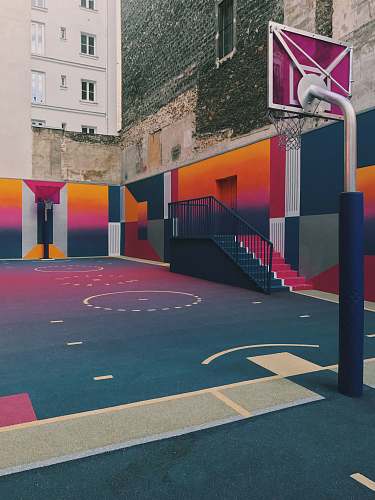 basketball black, purple, and orange basketball court beside concrete buildings at daytime basketball court