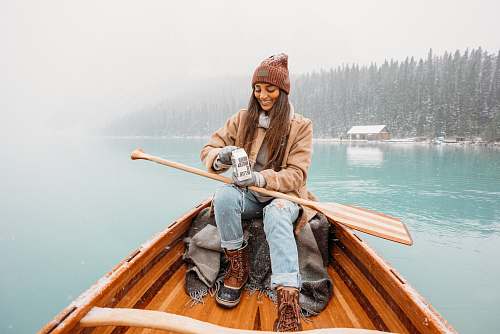 canoe man in brown jacket and blue denim jeans sitting on brown wooden boat during daytime rowboat