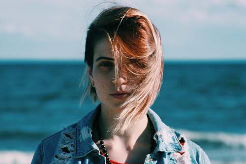 people woman in brown denim jacket standing near on beach during daytime shallow focus photography woman