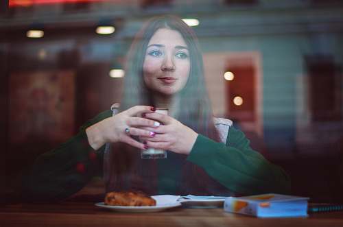 person woman in green sweater sitting in front of table holding drinking glass people