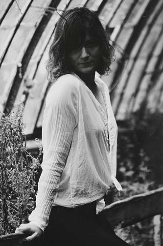 person grayscale photo of woman leaning on fence black-and-white