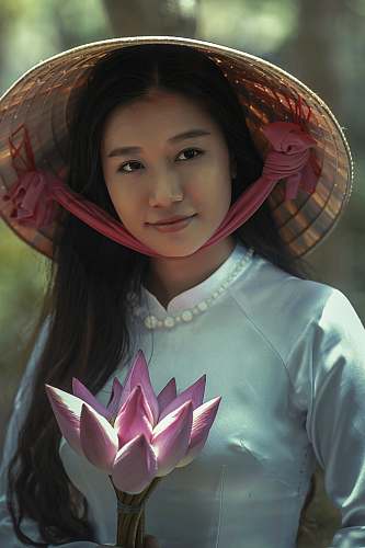 woman woman wearing white long-sleeved dress and brown sungat holding pink petaled flower female