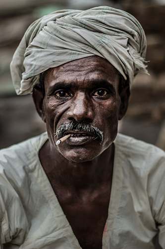 face man wearing gray turban smoking cigarette in closeup photography turban