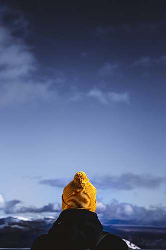 hat person wearing brown bobble hat facing cloudy skies buddha