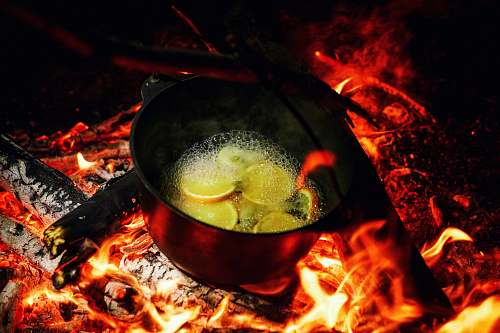 flame dutch oven on lit firewood with water and slices of fruits bonfire