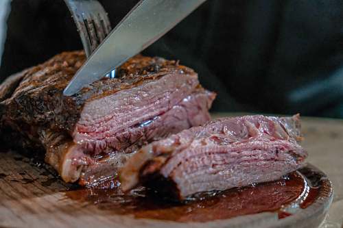 bbq person slicing juicy medium rare meat on top of brown wooden cutting board argentina