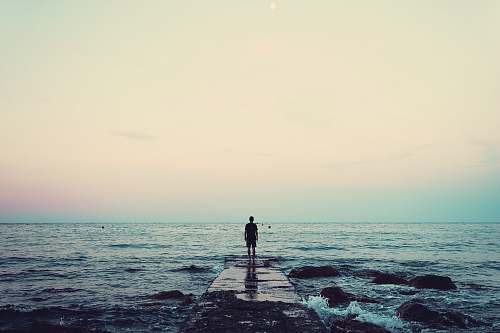 water silhouette of person standing on sea dock under cloudy sky ocean