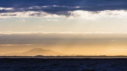 sky silhouette of road and mountain under gray clouds at golden hour water