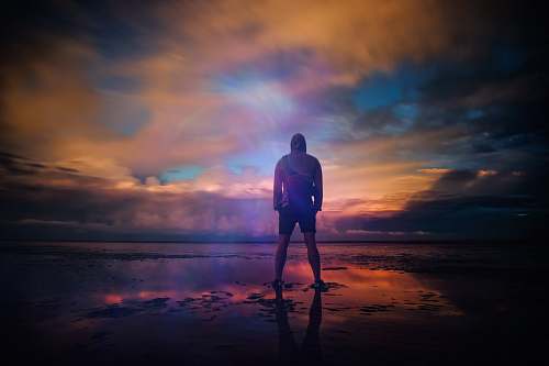 person A man standing triumphant on a beach in New Romney while looking out into the water people