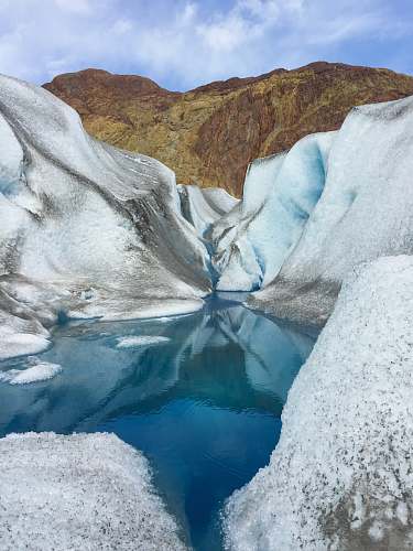 glacier brown rock mountain and lake with snow during daytime ice