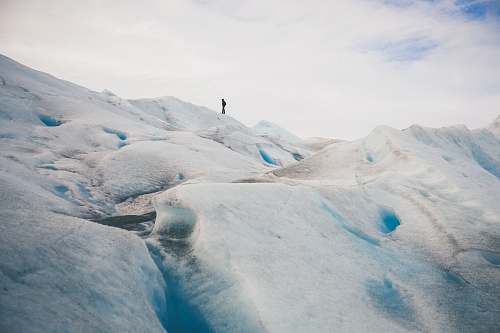 ice person standing on top of hill under white cloud blue skies glacier