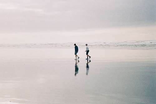 human two person walking at beach during daytime black-and-white